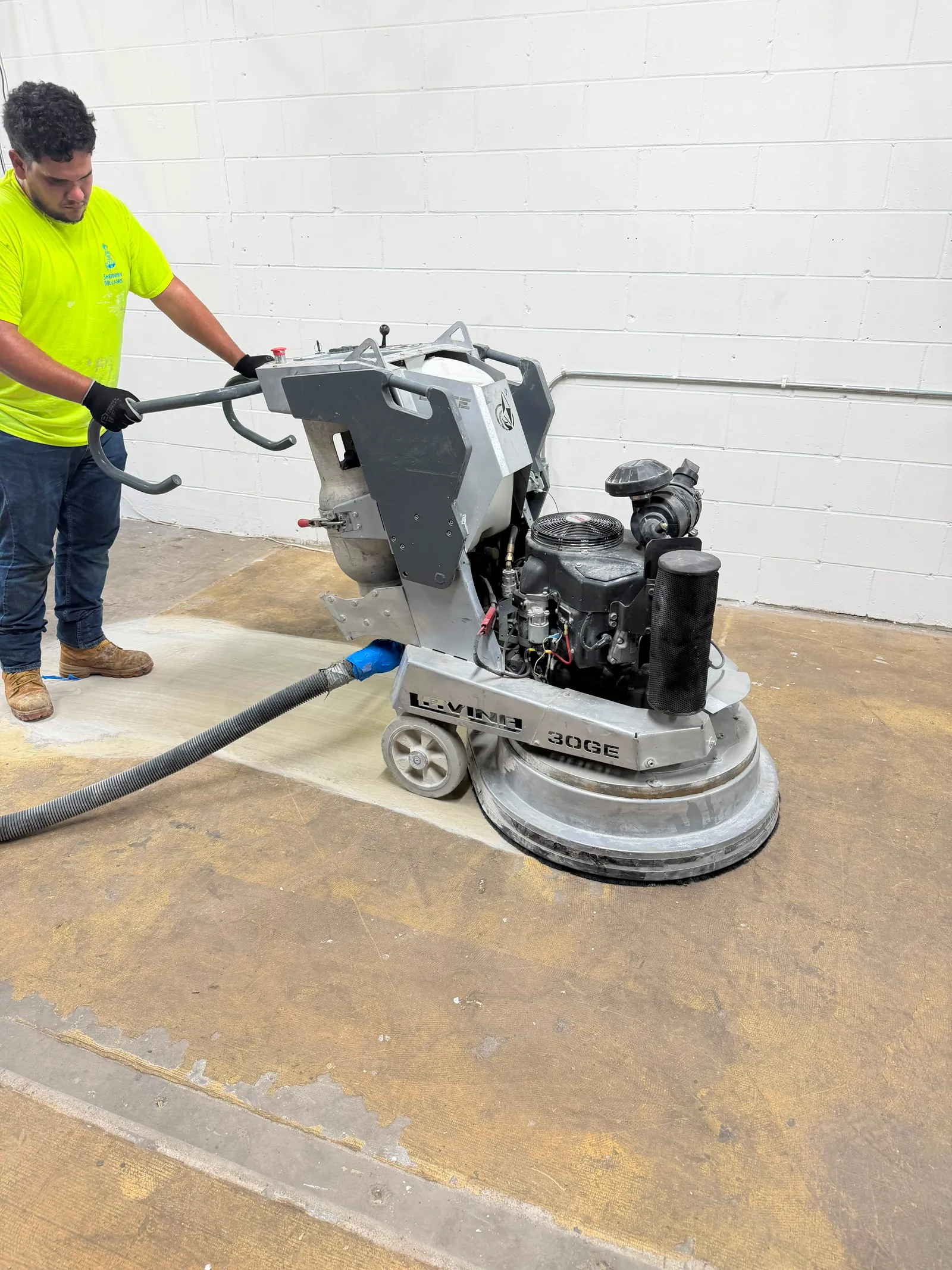 Technician diamond-grinding a concrete floor with a walk-behind grinder during surface preparation